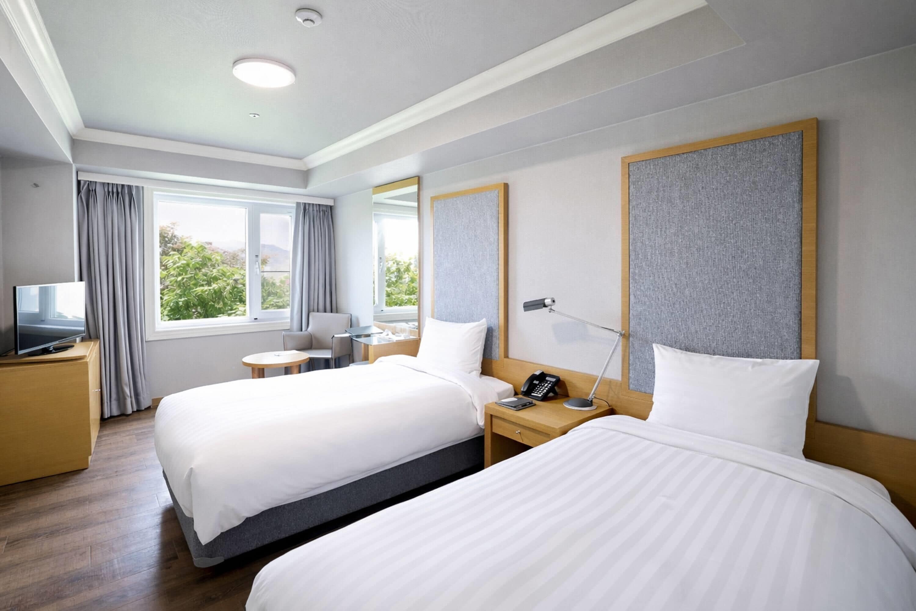 A hotel room with two beds, a desk, a chair, a TV, and a window with curtains.
