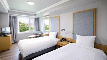 A hotel room with two beds, a desk, a chair, a TV, and a window with curtains.