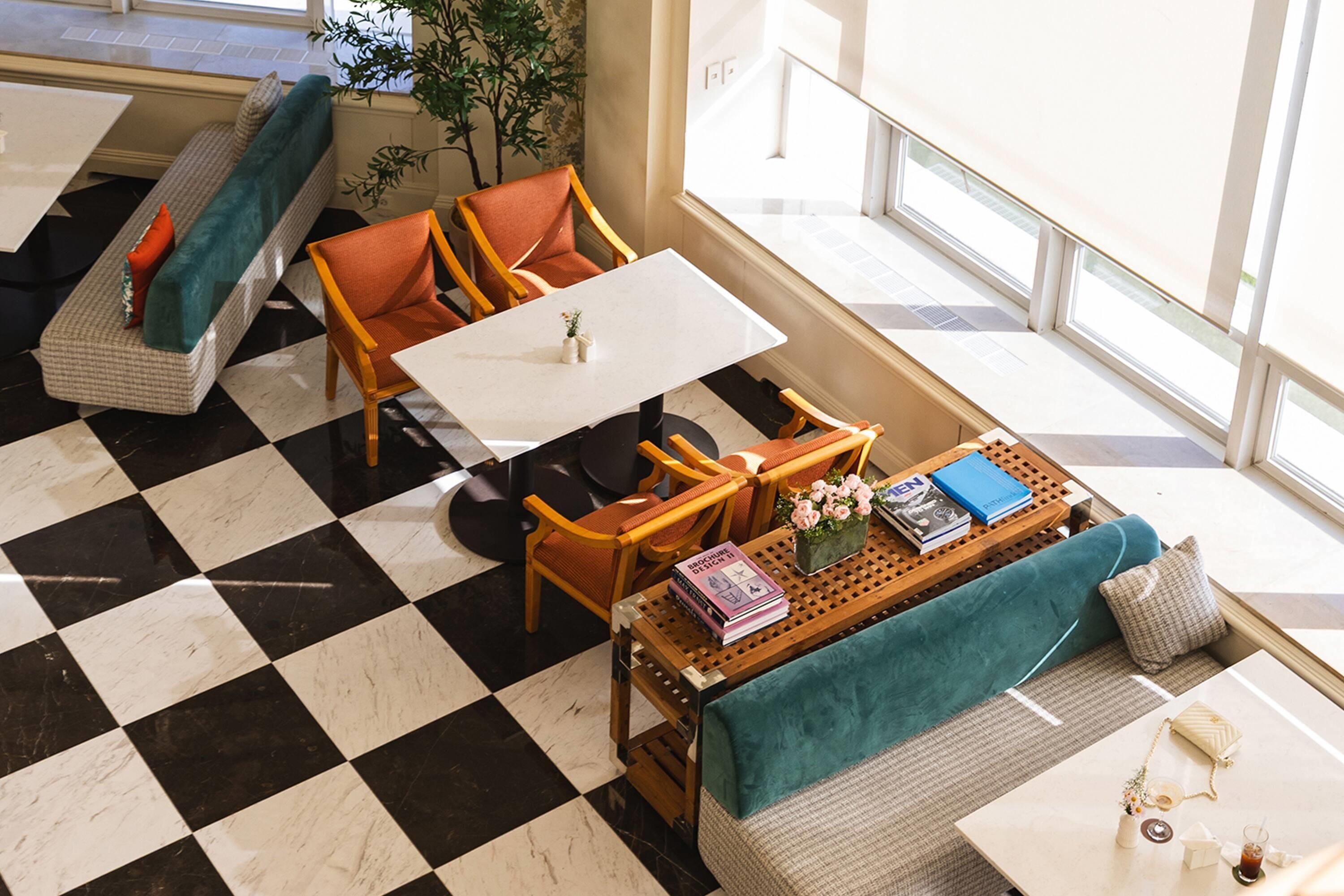 A checkered floor, a white table, a teal sofa, and wooden chairs in a bright room with windows.