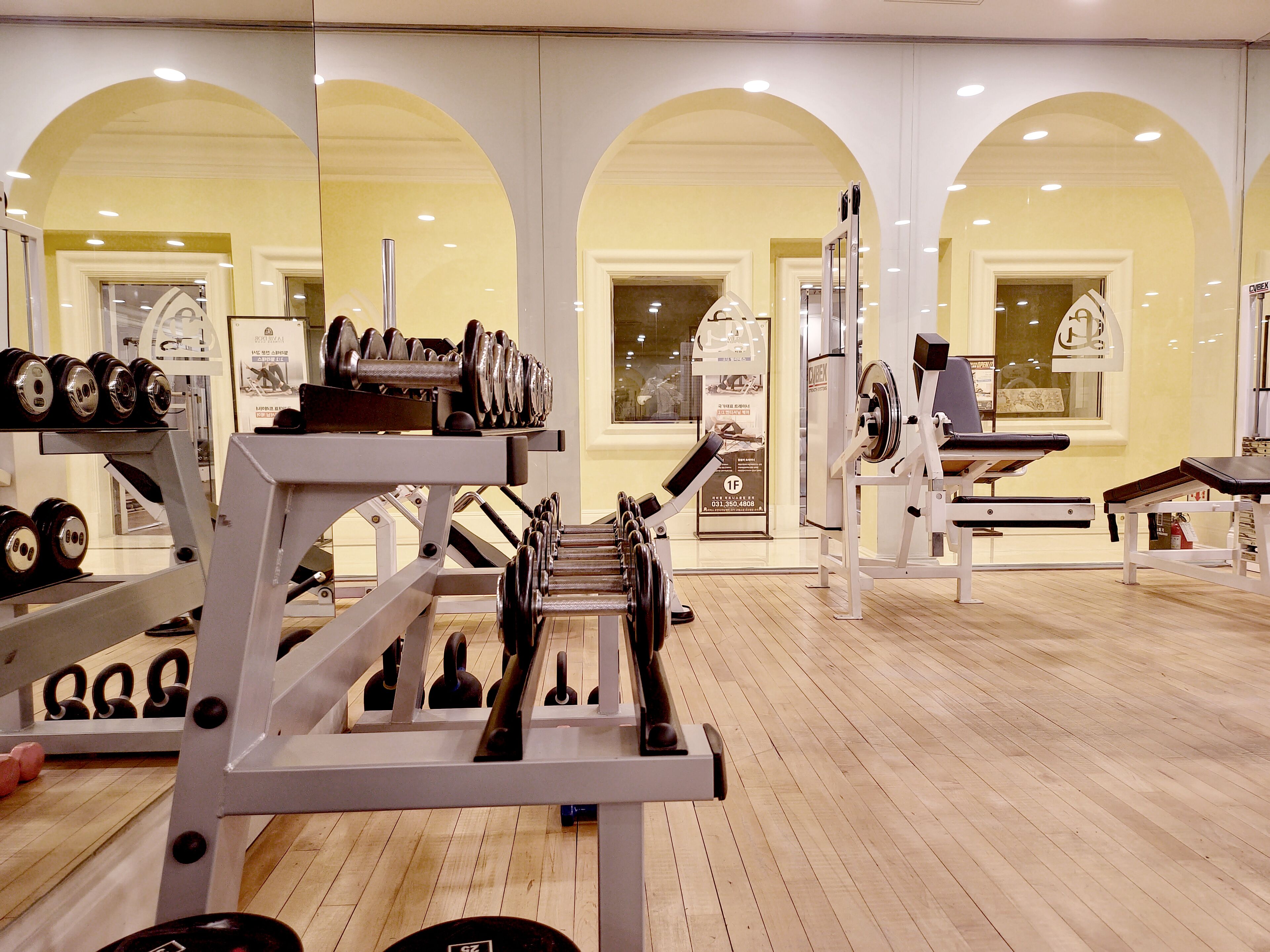 A gym with various exercise equipment, wooden flooring, and arched ceilings.