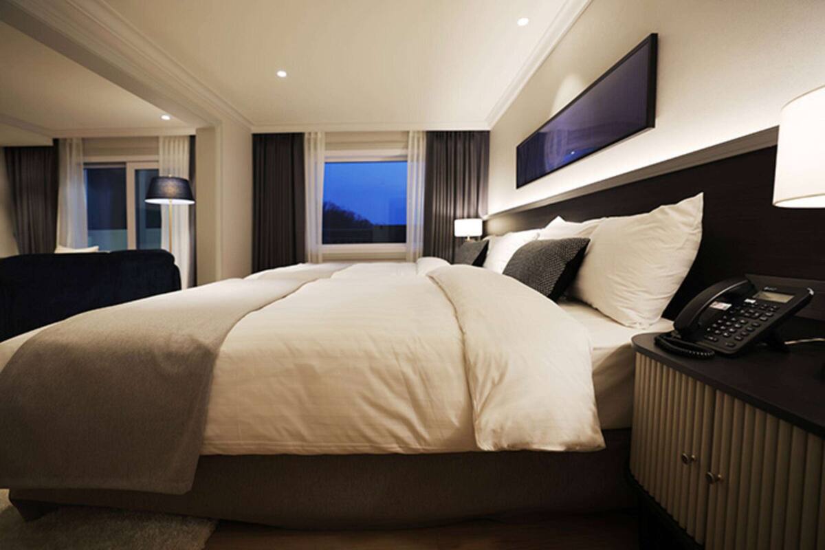 A hotel room with a large bed, bedside tables, a flat-screen TV, and a window with curtains.