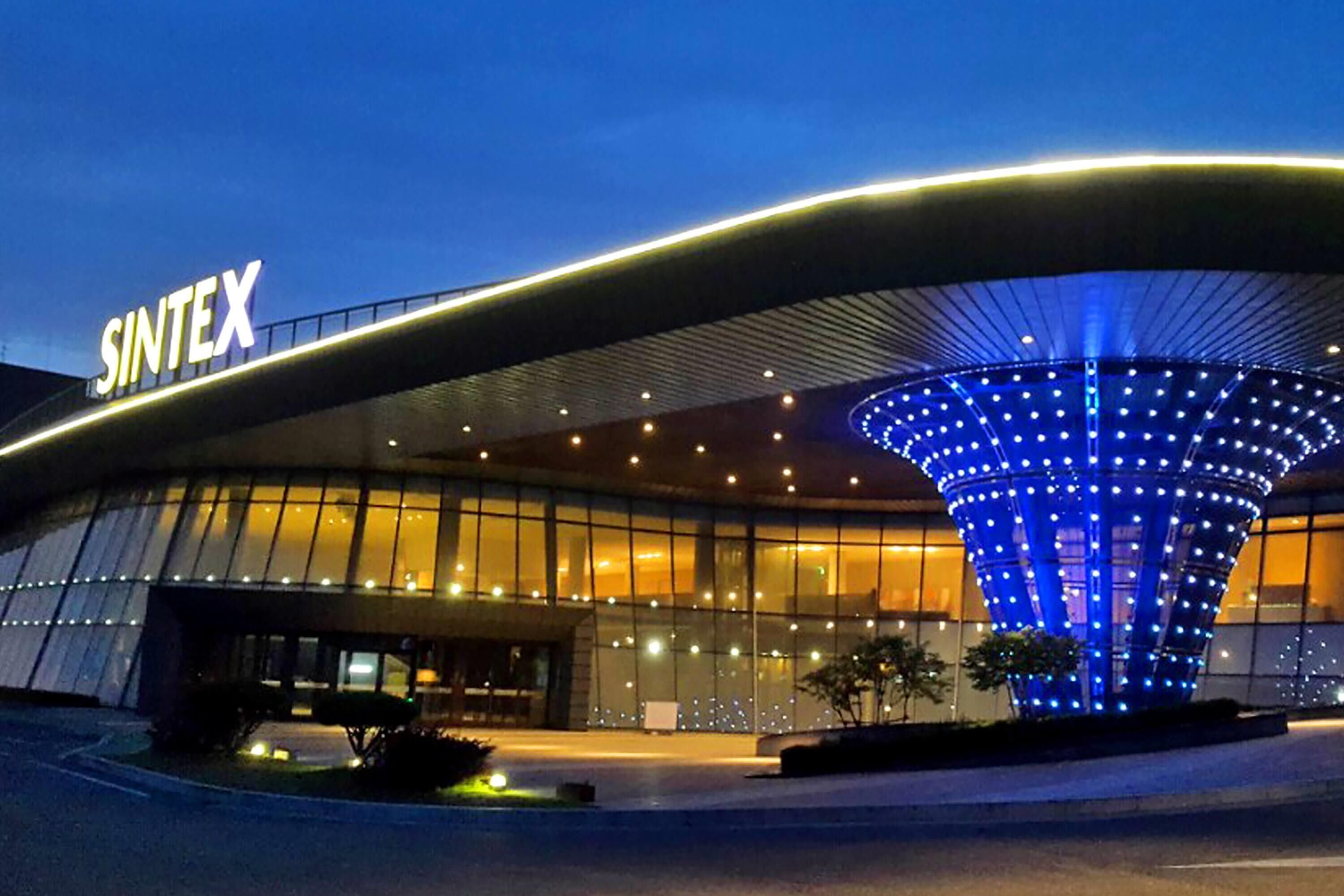 A modern building with a curved roof and a large, illuminated blue structure in front.