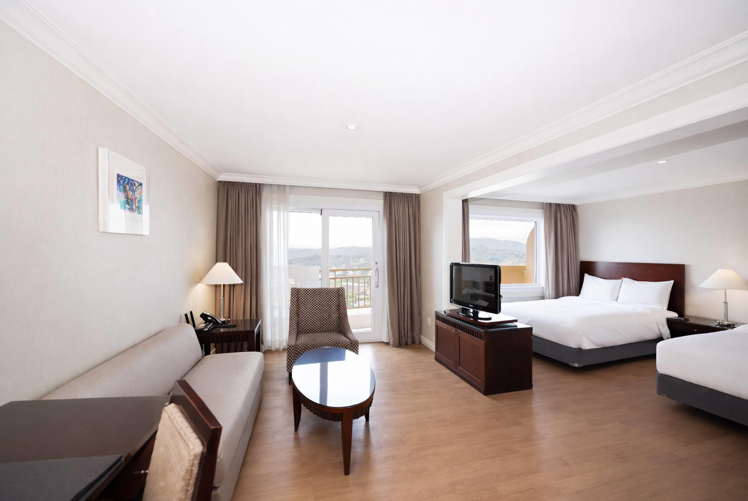Quarto de hotel com sofá, mesa redonda, televisão, cama e vista para o exterior.