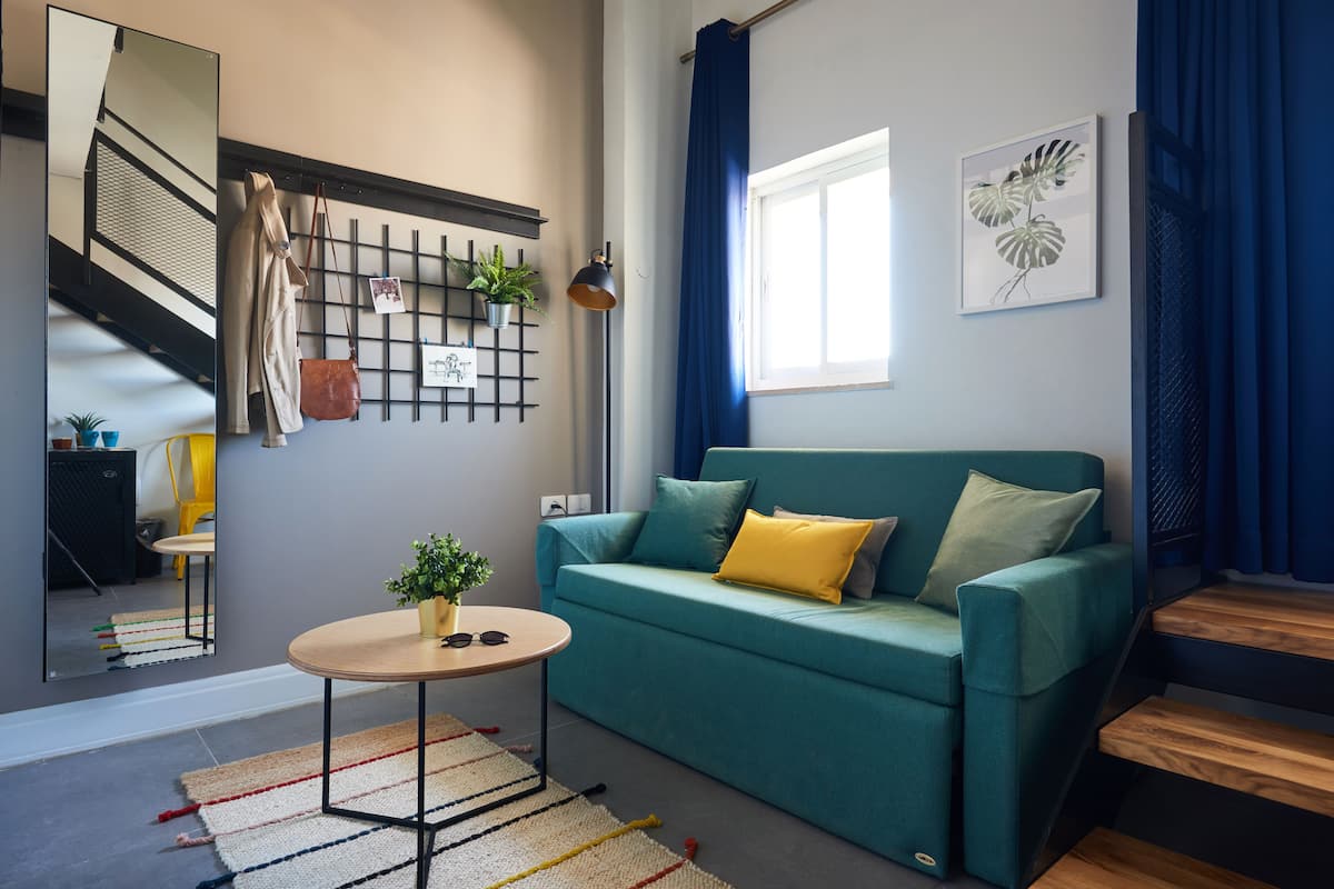 A modern living room with a teal sofa, a round wooden coffee table, and a mirror reflecting the room.