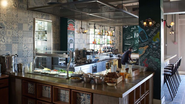 A kitchen area with a bar counter, various kitchen appliances, and a chalkboard wall with writing. - The Post Hostel (Jerusalem)