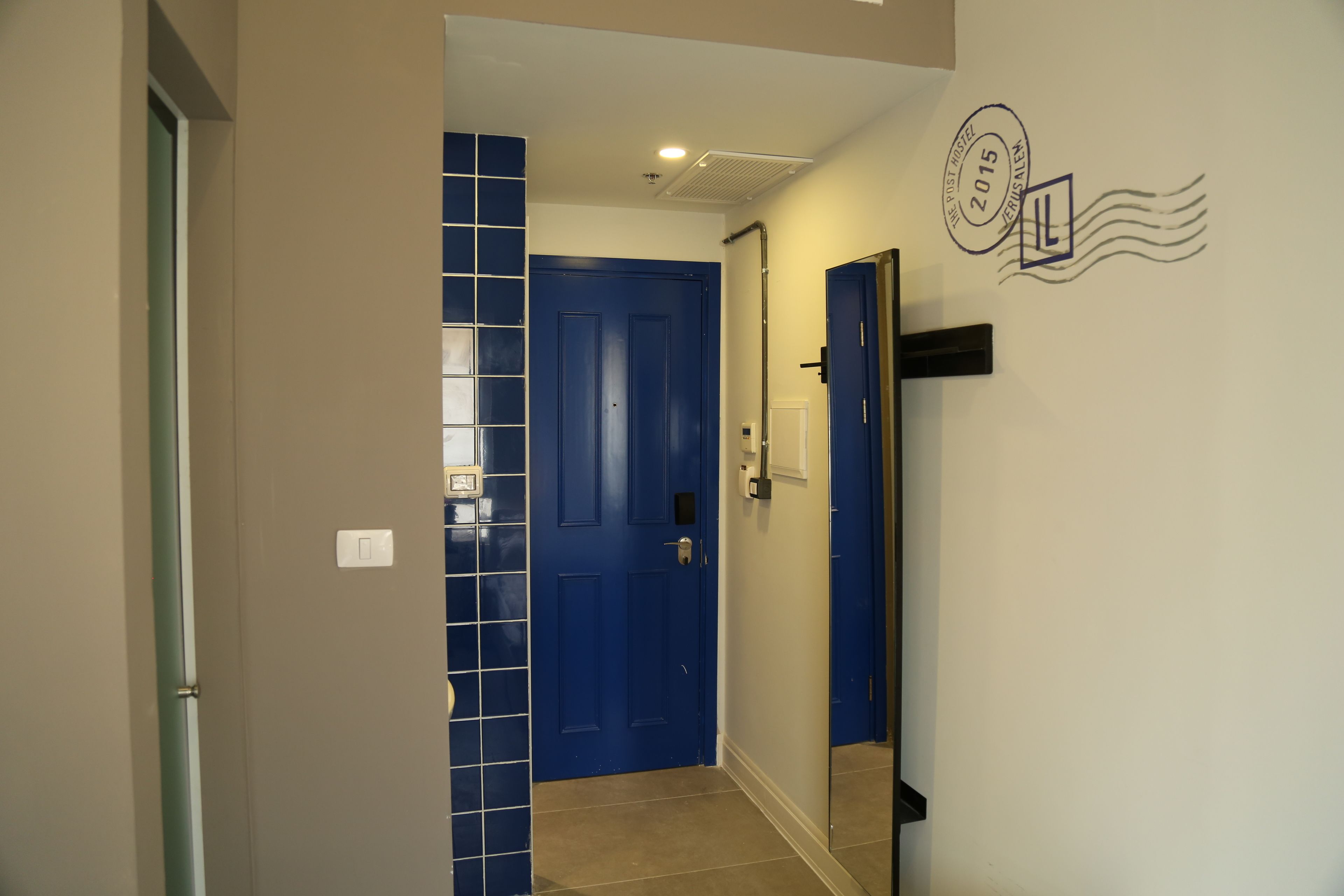 A hallway with a blue door, a white wall with a postmark stamp, and a mirror reflecting part of the room.