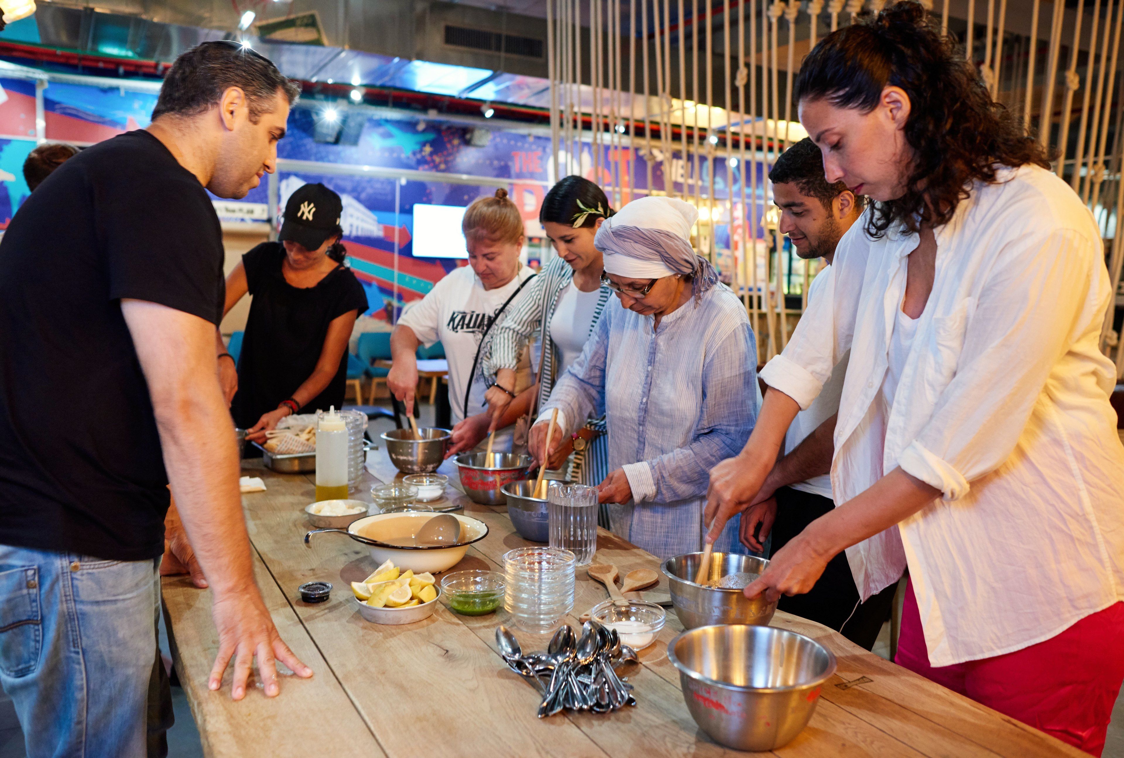 A group of people preparing food at a wooden table with various utensils and containers.