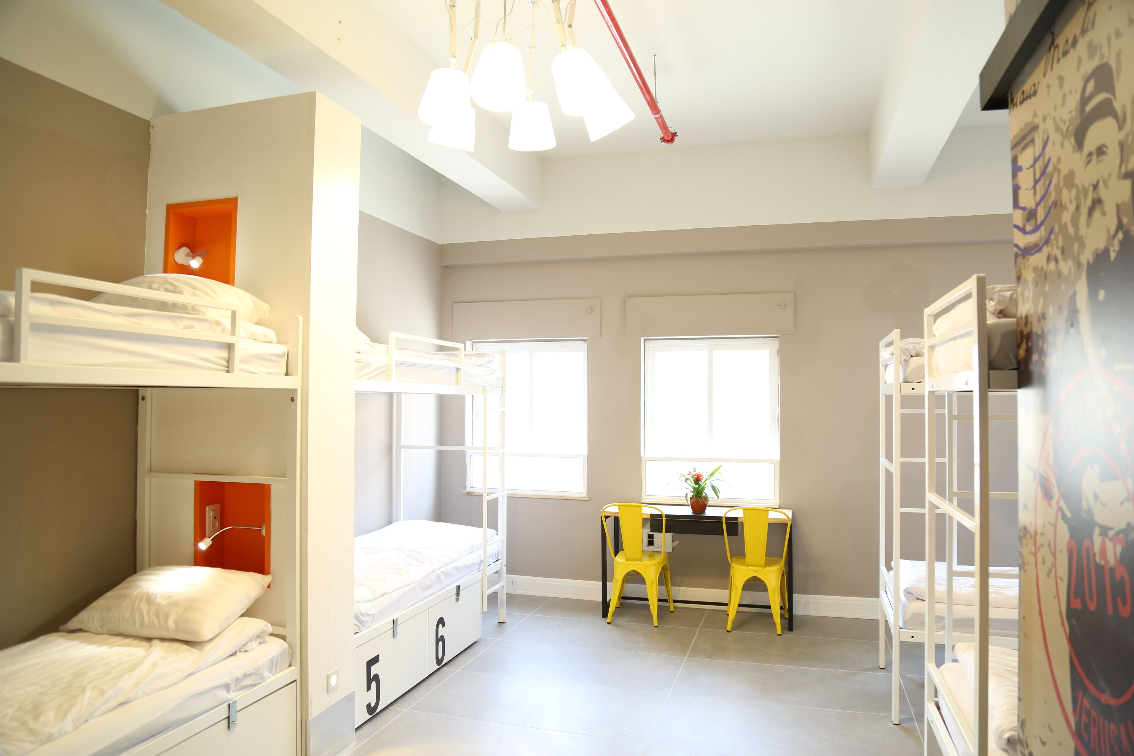 A dormitory room with bunk beds, a desk, chairs, and a window.