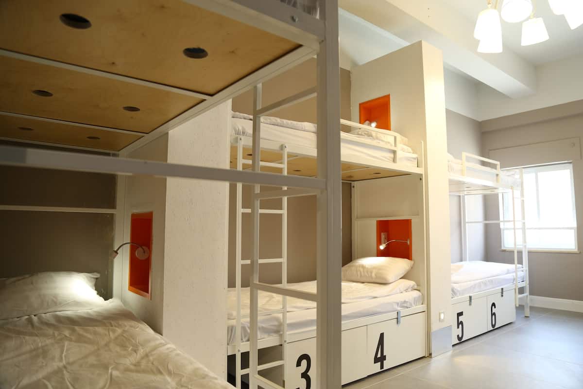 A bunk bed room with a wooden ceiling, white beds, and a window with natural light.