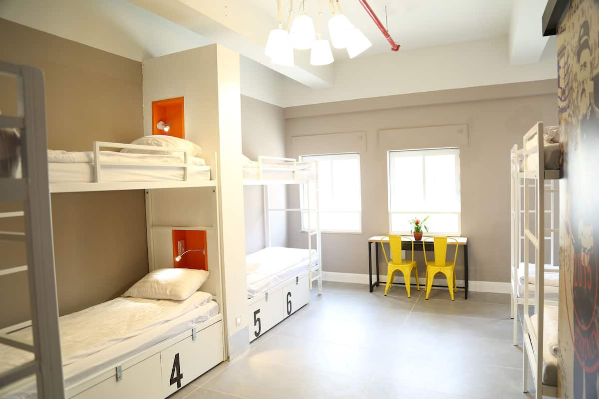 A dormitory room with bunk beds, a desk, and chairs.