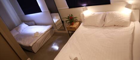 Une chambre d’hôtel avec un grand lit, un lit plus petit, une table de chevet avec une plante et un miroir.