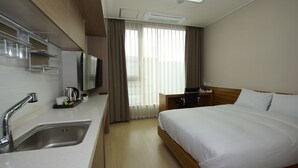 Ein Hotelzimmer mit Bett, Schreibtisch, Fernseher, Spüle und einem Fenster mit Vorhängen.