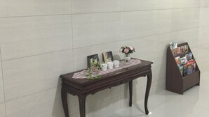 Ein Empfangstresen mit dem Schild 'C+plus RESIDENCE' darüber, ein kleiner Tisch mit Blumenvase und ein Magazinständer.