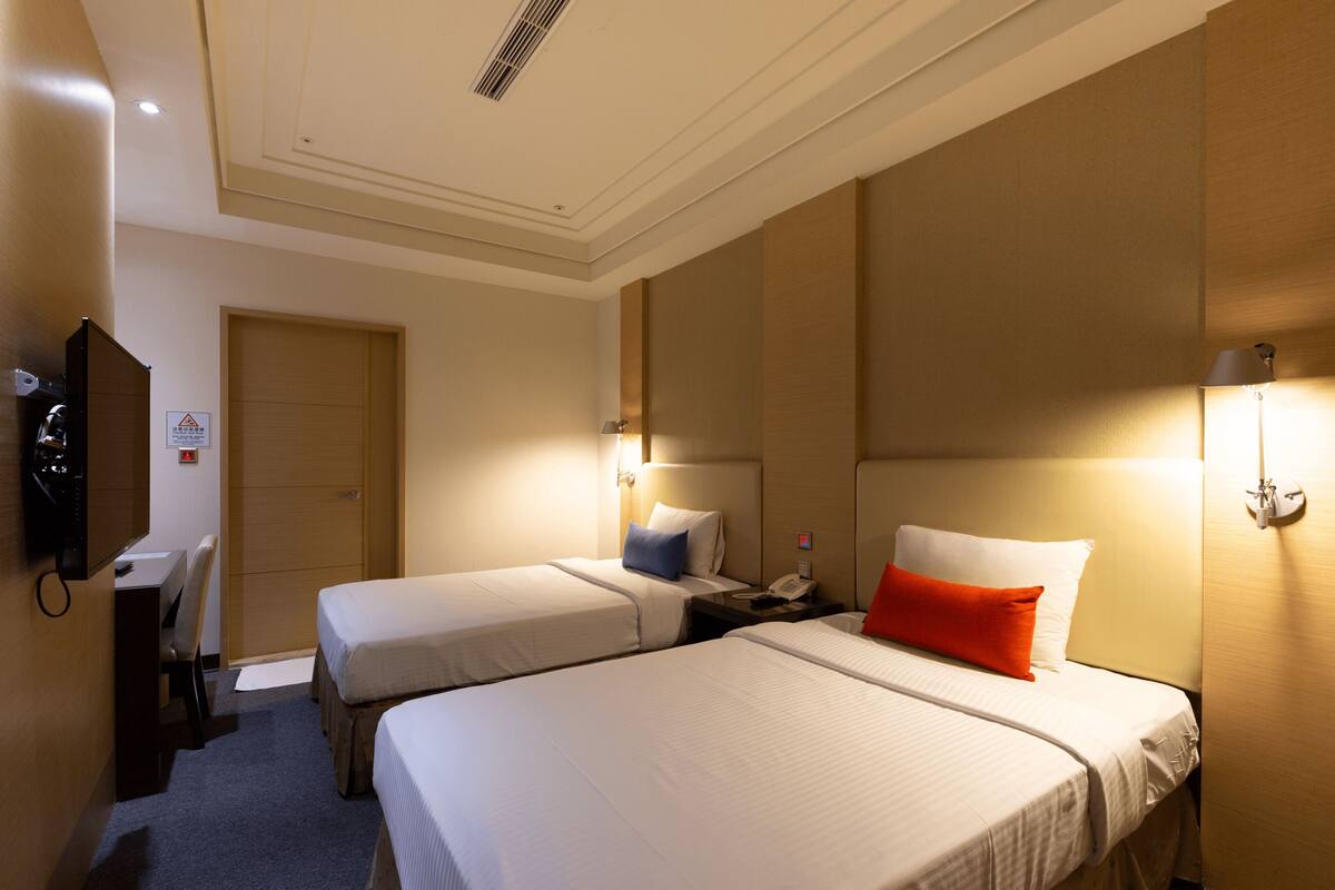 Ein Hotelzimmer mit zwei Betten, einem Schreibtisch, einem Stuhl, einem Fernseher und einer Tür.