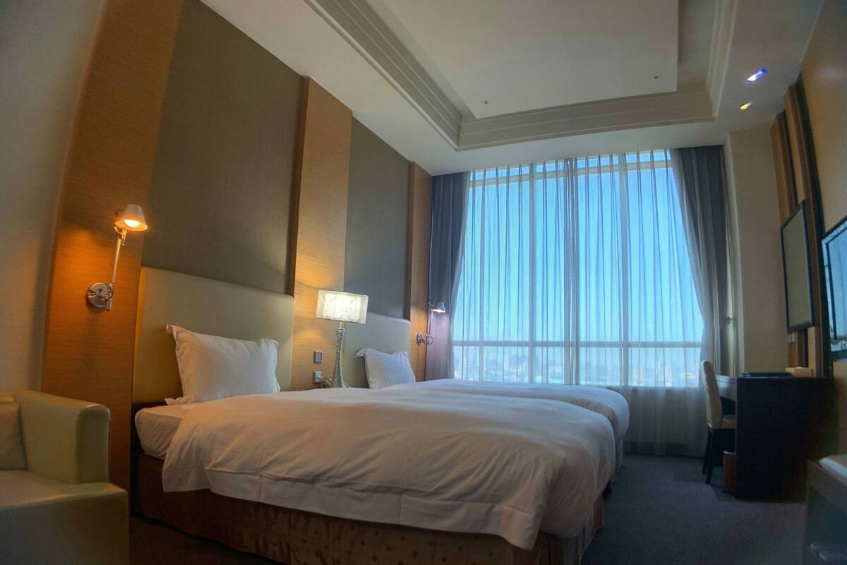 Ein Hotelzimmer mit einem großen Bett, zwei Nachttischlampen, einem Schreibtisch und einem Stuhl.