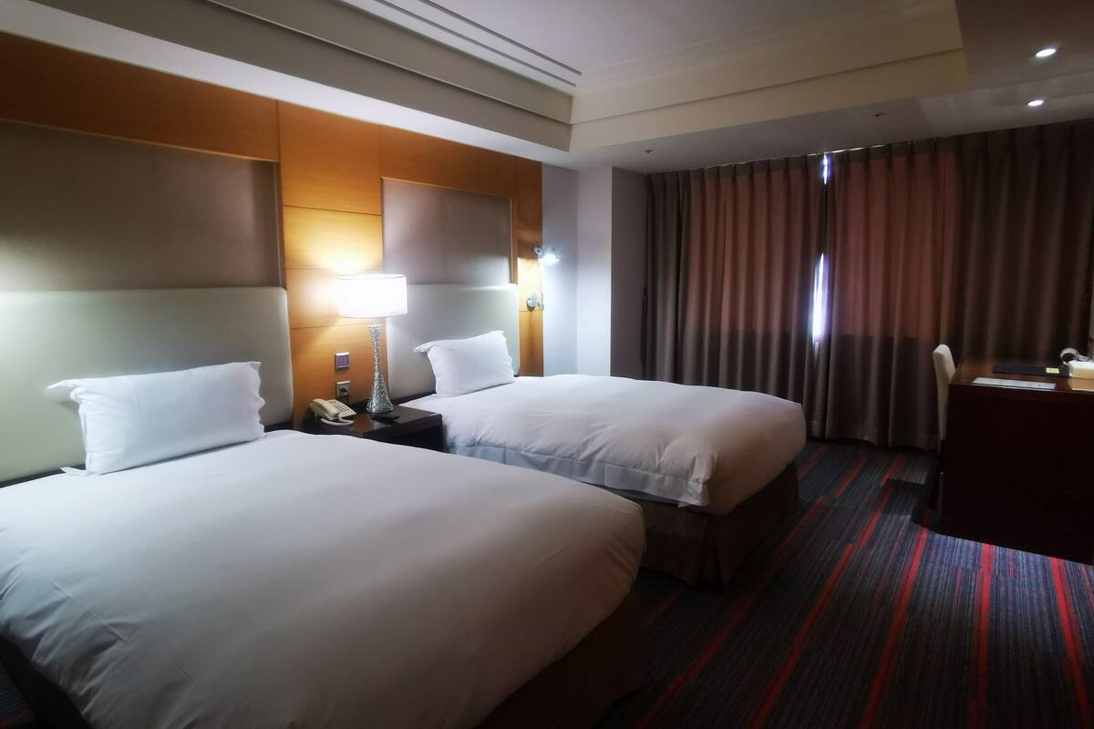 Ein Hotelzimmer mit zwei Betten, einem Schreibtisch, einer Lampe und Blick aus dem Fenster.
