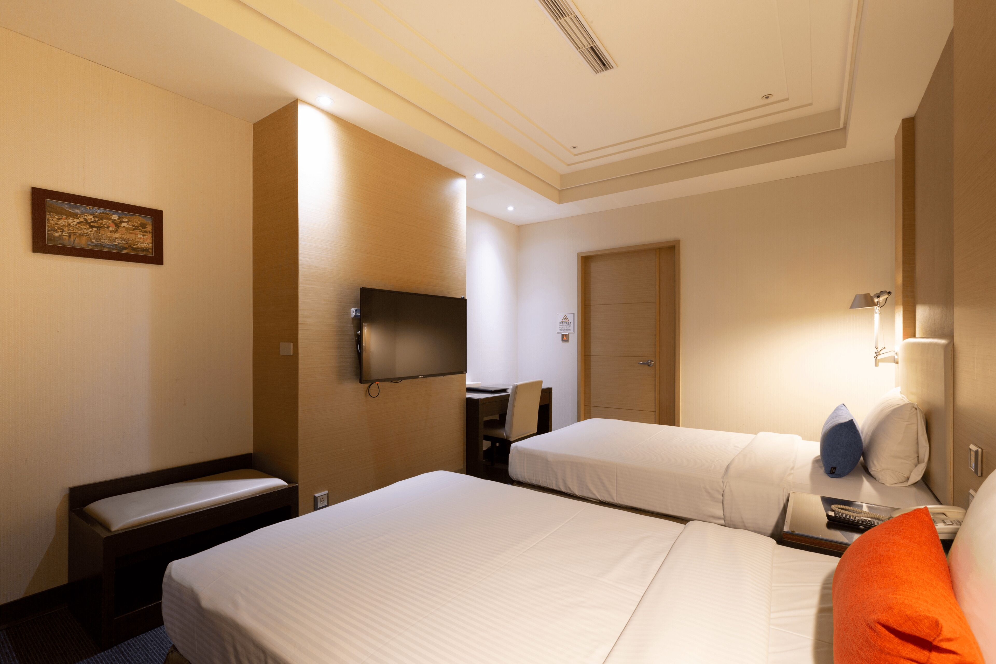 A hotel room with two beds, a desk, a chair, a television, and a door.