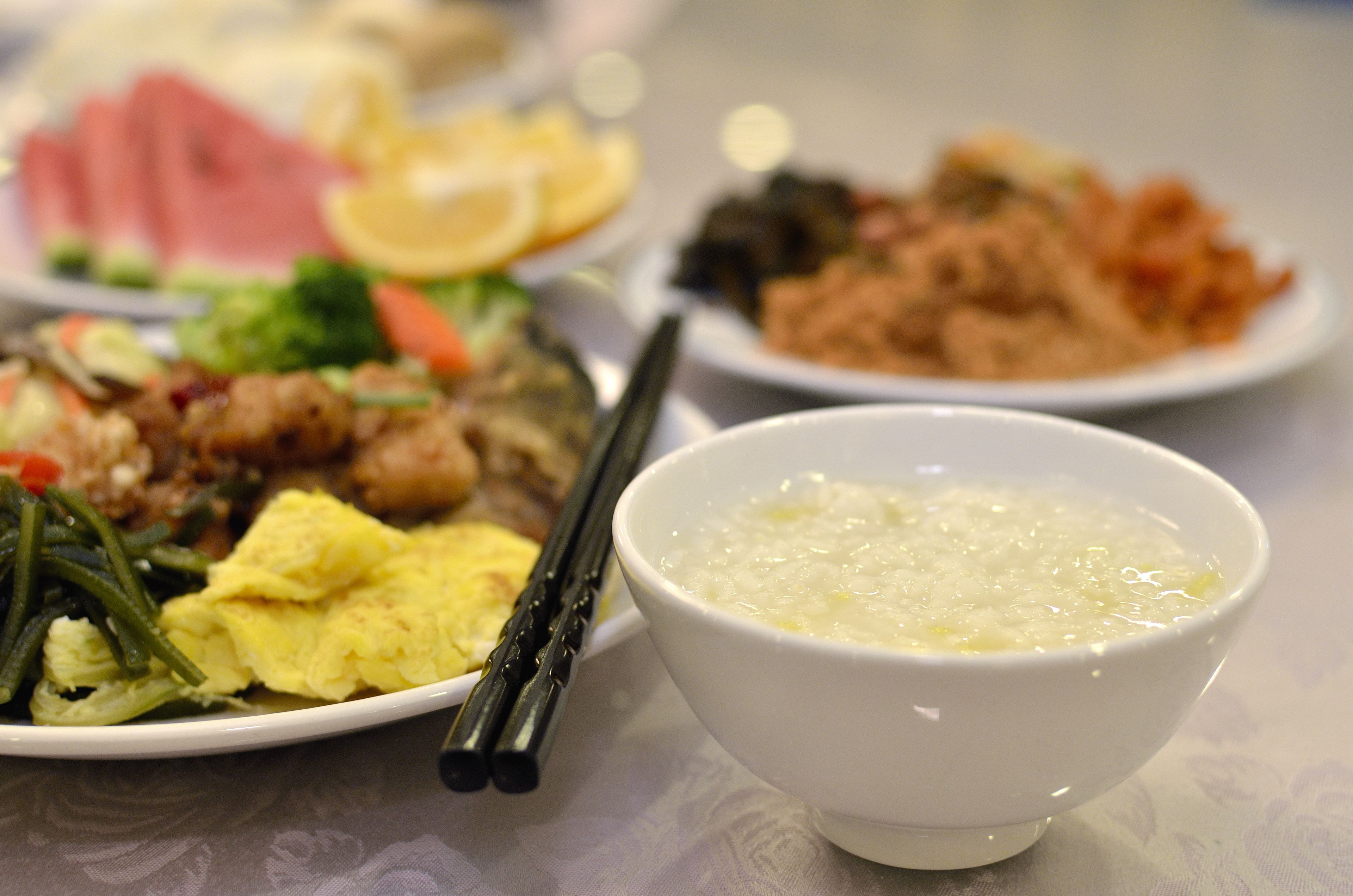 Una mesa con diferentes platos, incluyendo un bol de sopa, un plato con verduras y carne, y un plato con arroz y verduras.