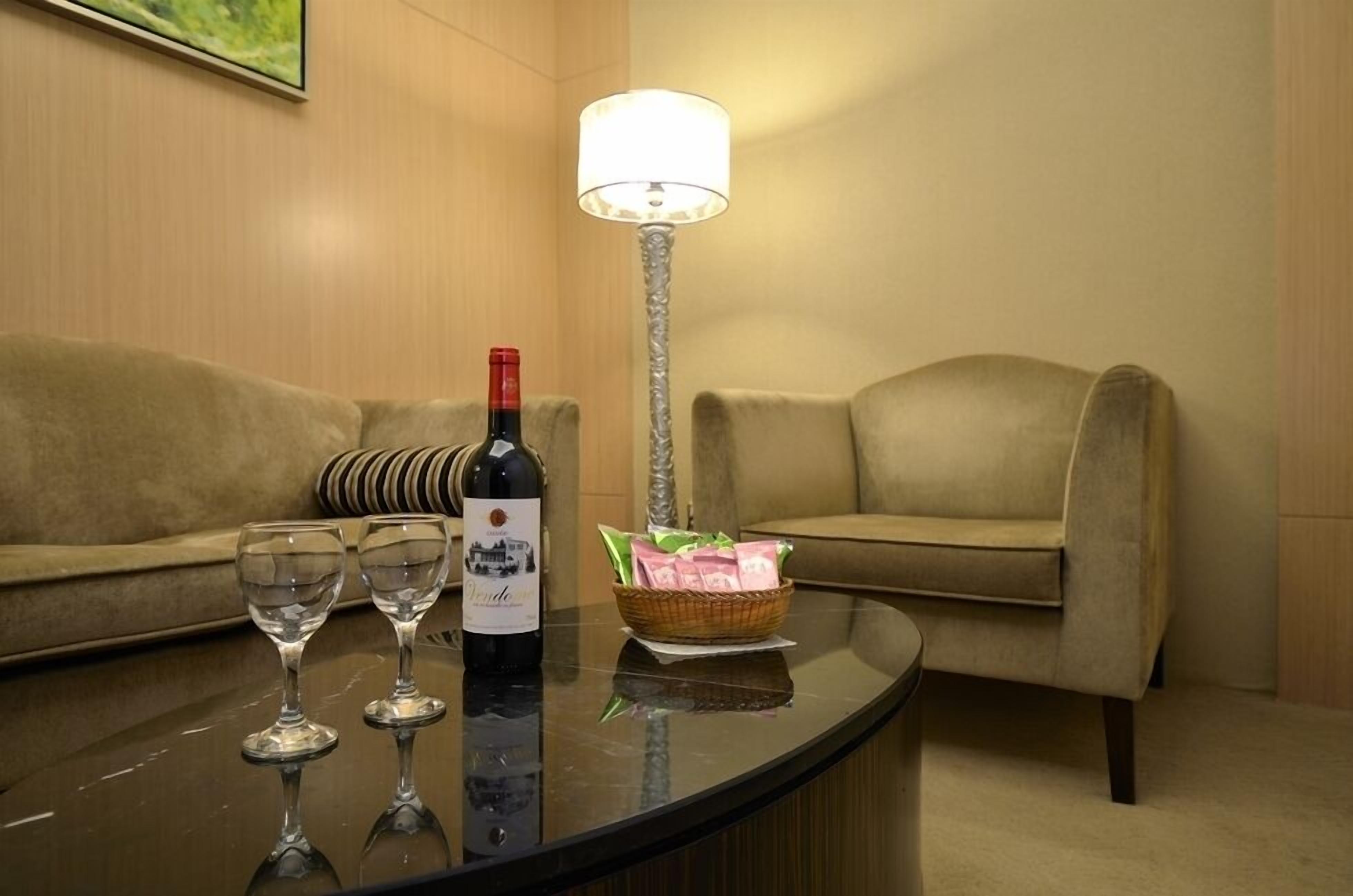 A room with a round table, a bottle of wine, two wine glasses, a lamp, and a basket of snacks.