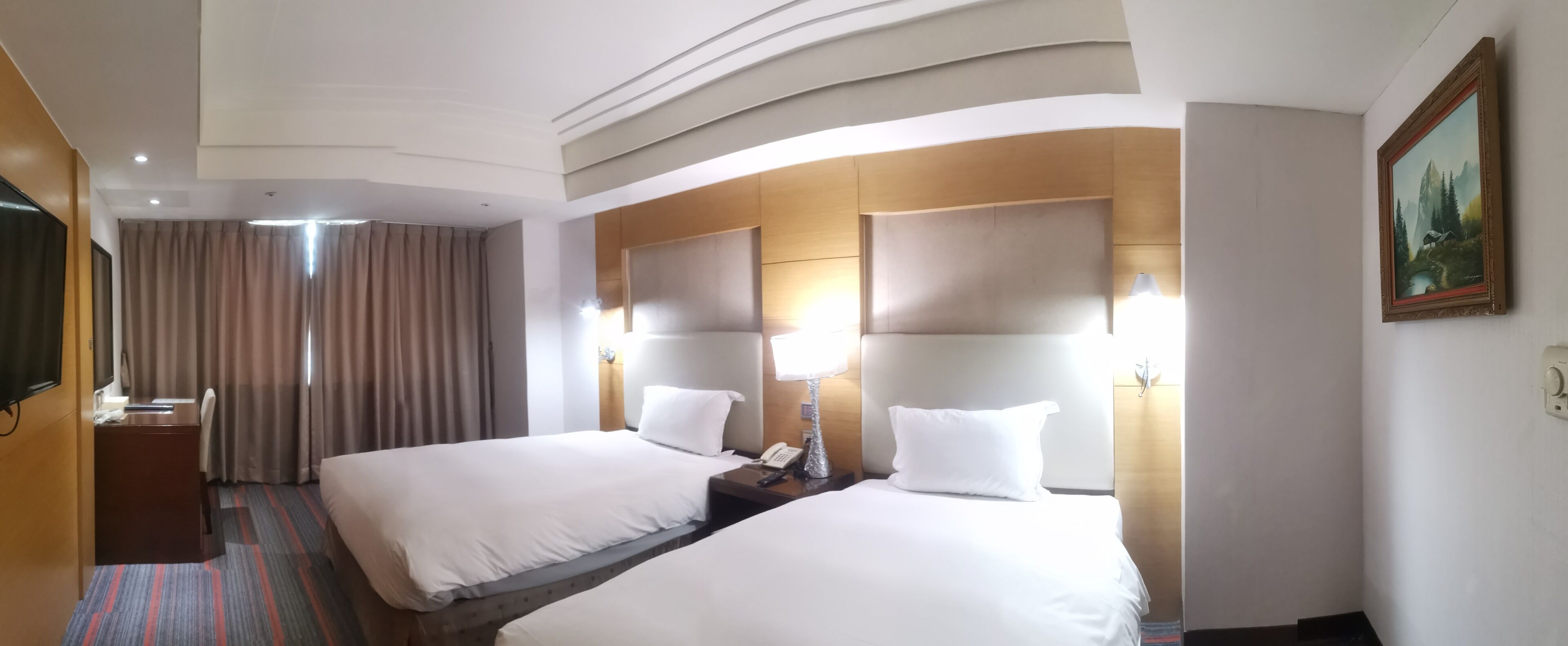 A hotel room with two beds, a desk, a TV, and a painting on the wall.