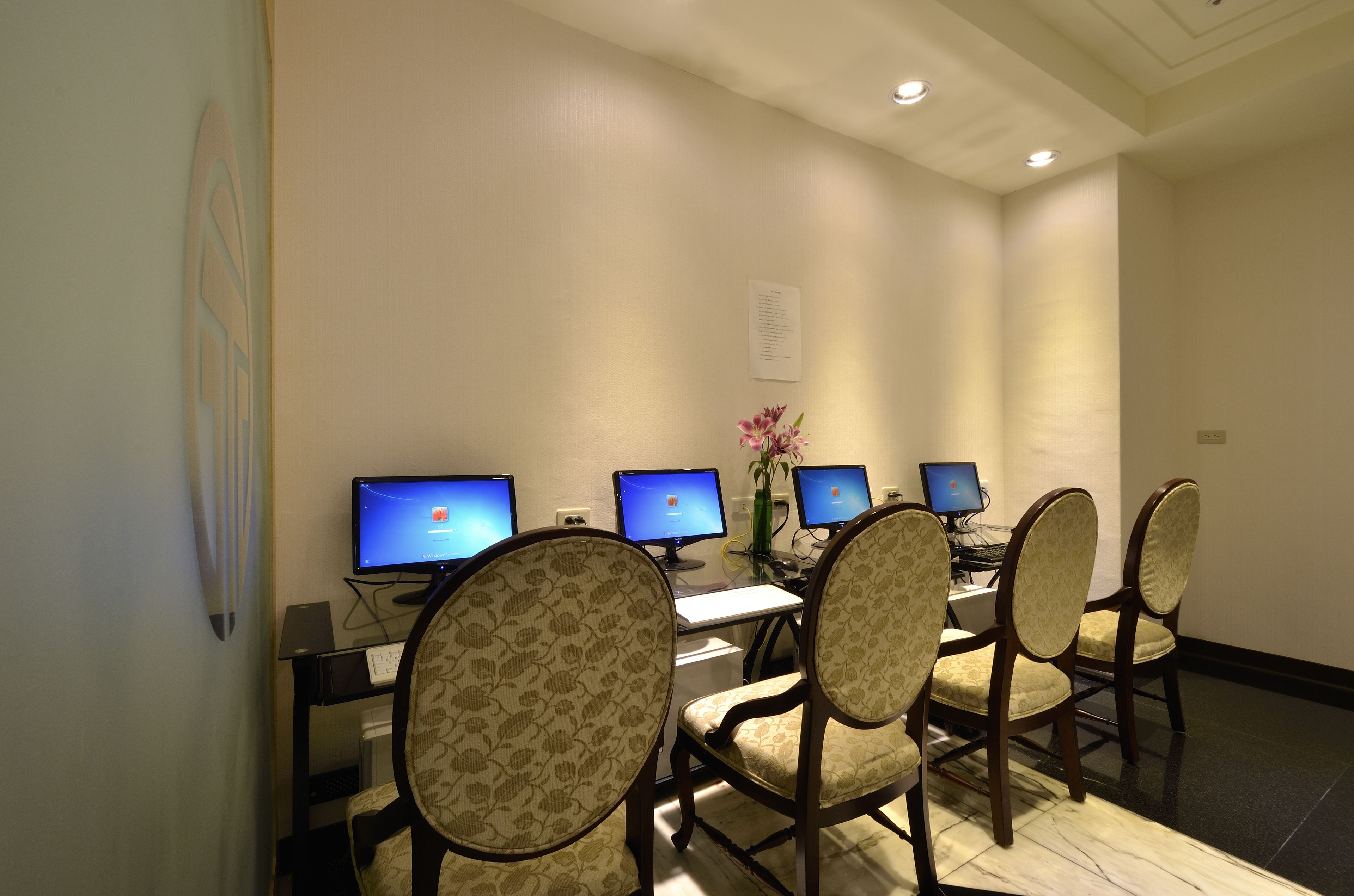 A conference room with four computer monitors, a whiteboard, and a desk with a vase of flowers.