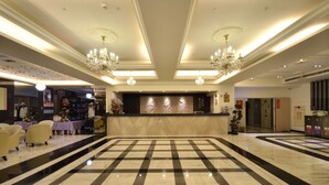A hotel lobby with a checkered floor, chandeliers, a reception desk, and seating areas.