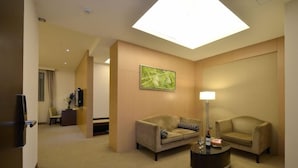 A hotel room with two sofas, a coffee table, a painting, and a desk with a lamp.