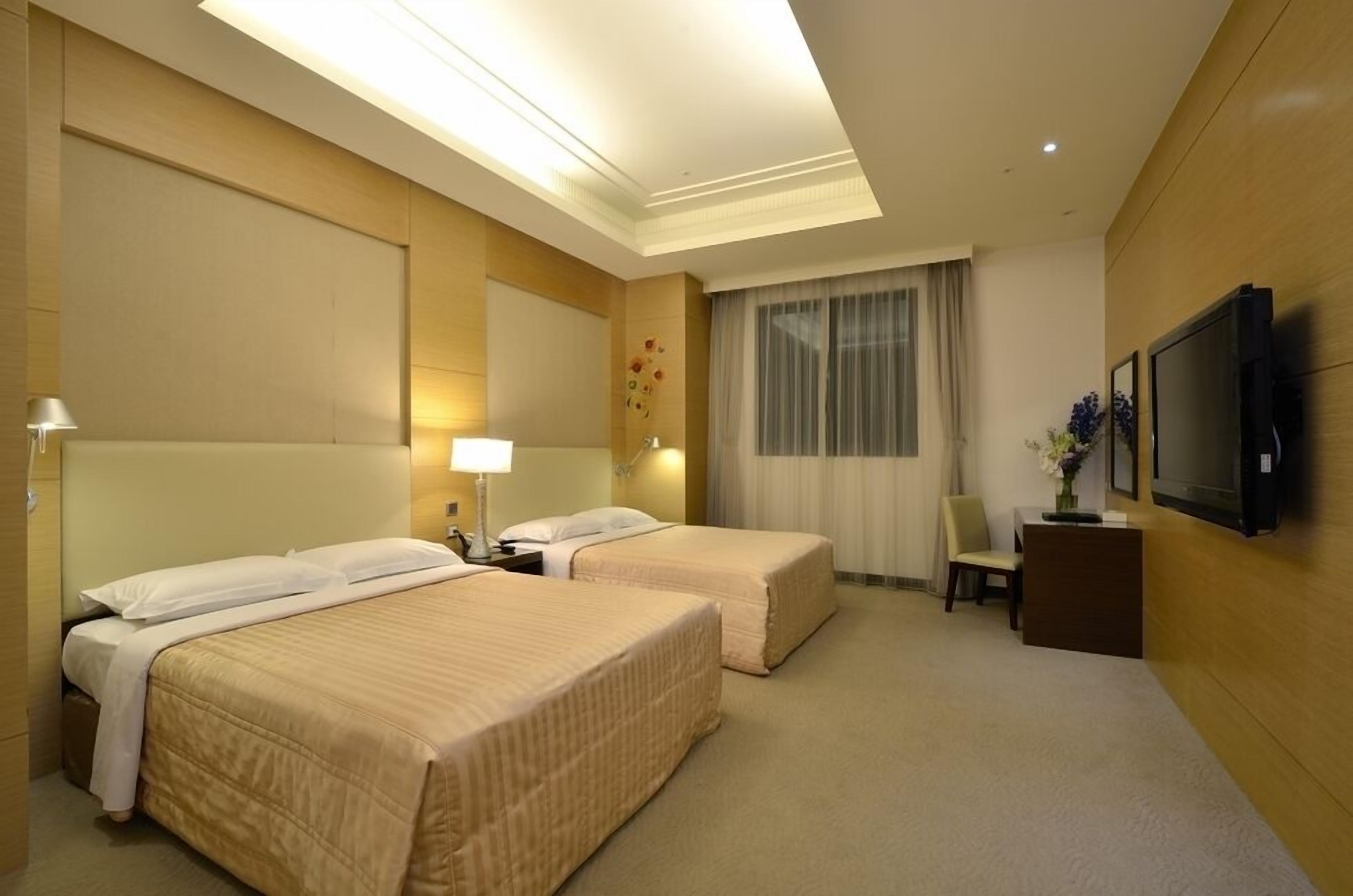 A hotel room with two beds, a desk, a chair, a TV, and a window with curtains.