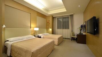 A hotel room with two beds, a desk, a chair, a TV, and a window with curtains.