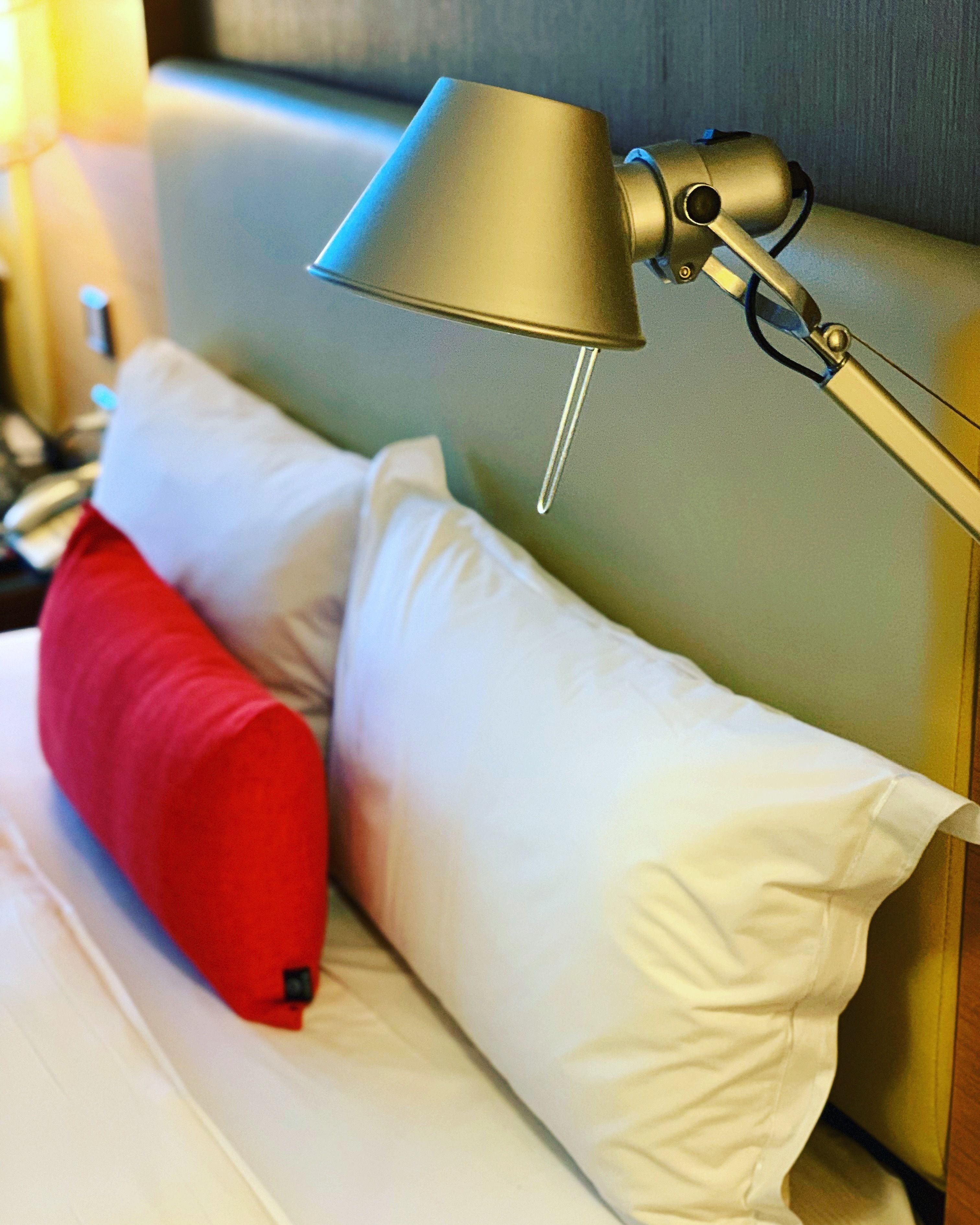 Una cama con almohadas blancas y rojas, una lámpara y un cabecero de madera.