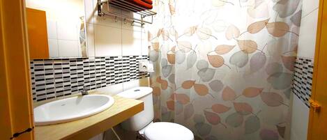 A bathroom with a white sink, a toilet, and a shower curtain with a leaf pattern.