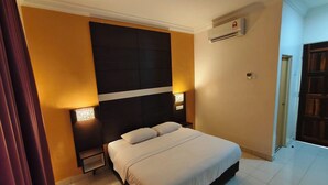 Ein Hotelzimmer mit einem großen Bett, zwei Nachttischen, einer Wand-Klimaanlage und einer Tür rechts.