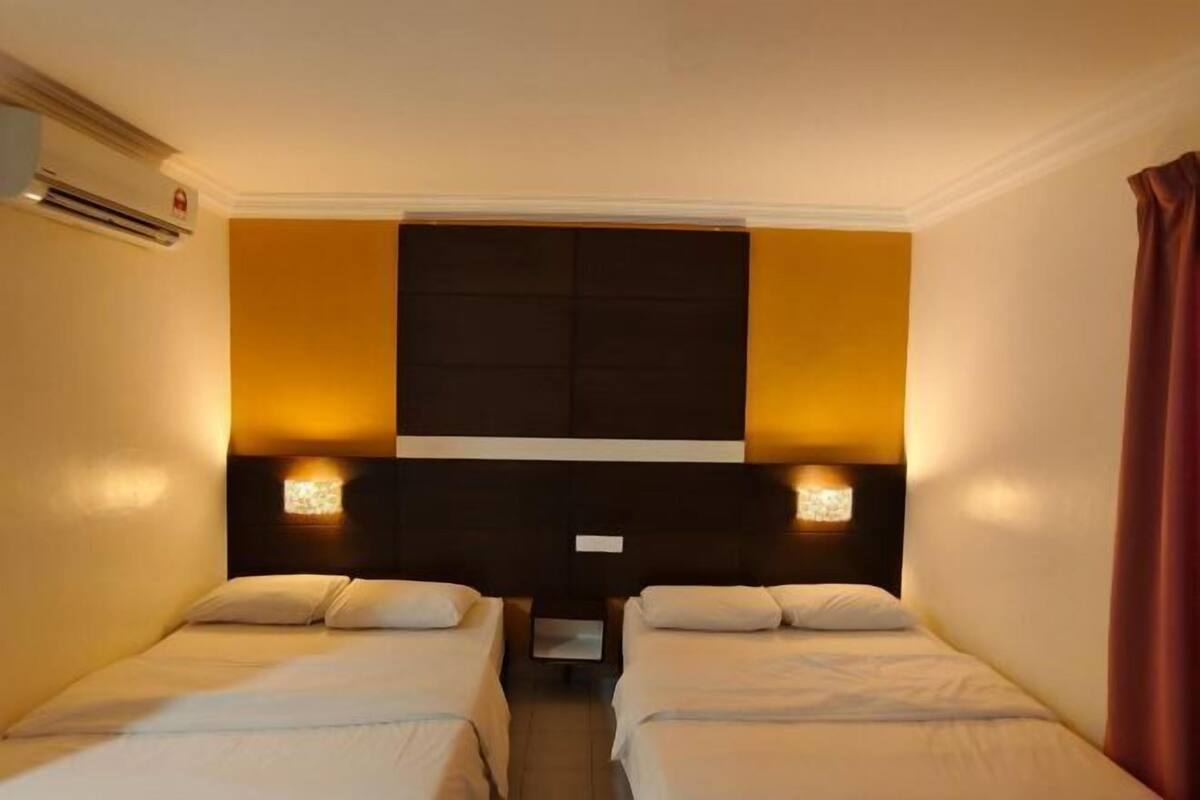 Habitación de hotel con dos camas, un cabecero grande y oscuro, e iluminación montada en la pared.