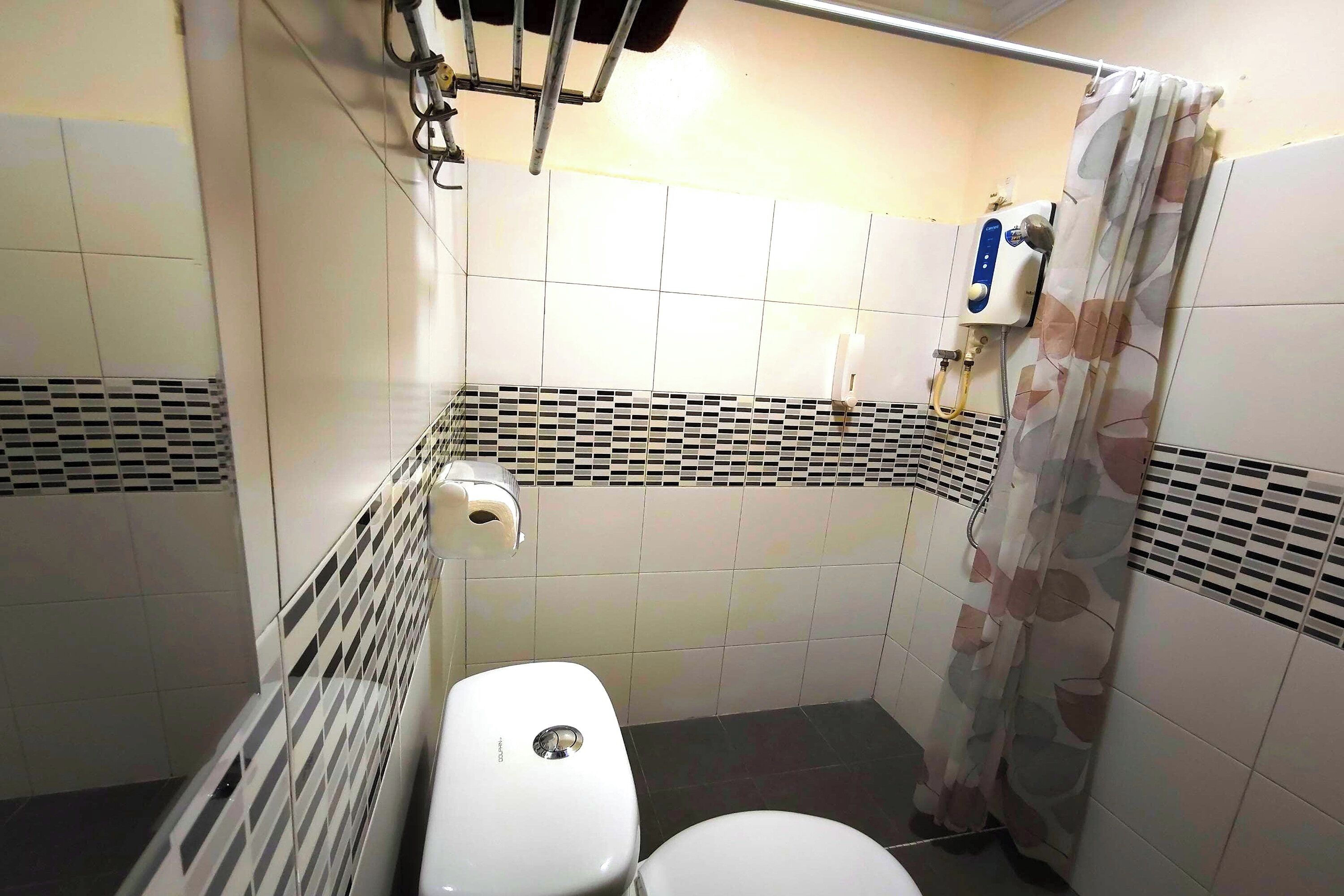 A small, tiled bathroom with a toilet, a shower curtain, and a hand dryer.