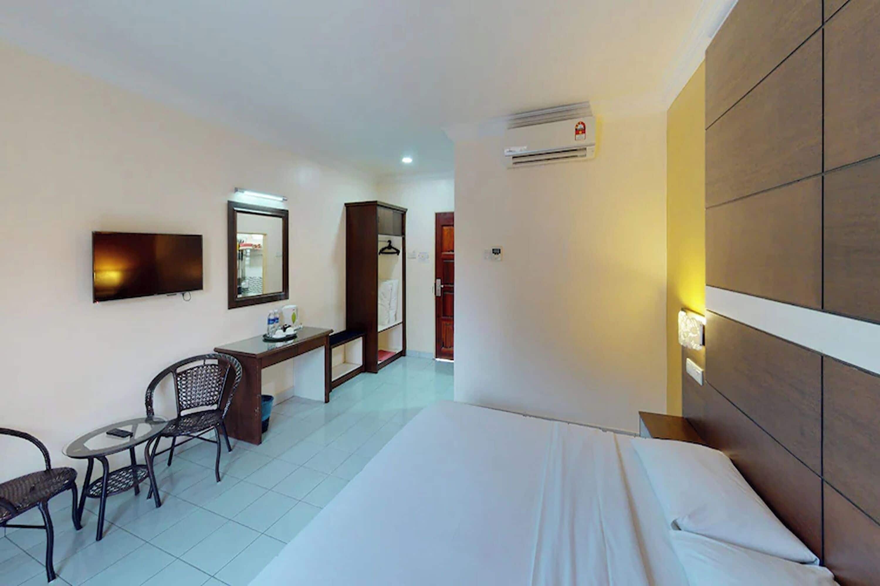 A hotel room with a bed, a desk with a chair, a TV, and a wardrobe.