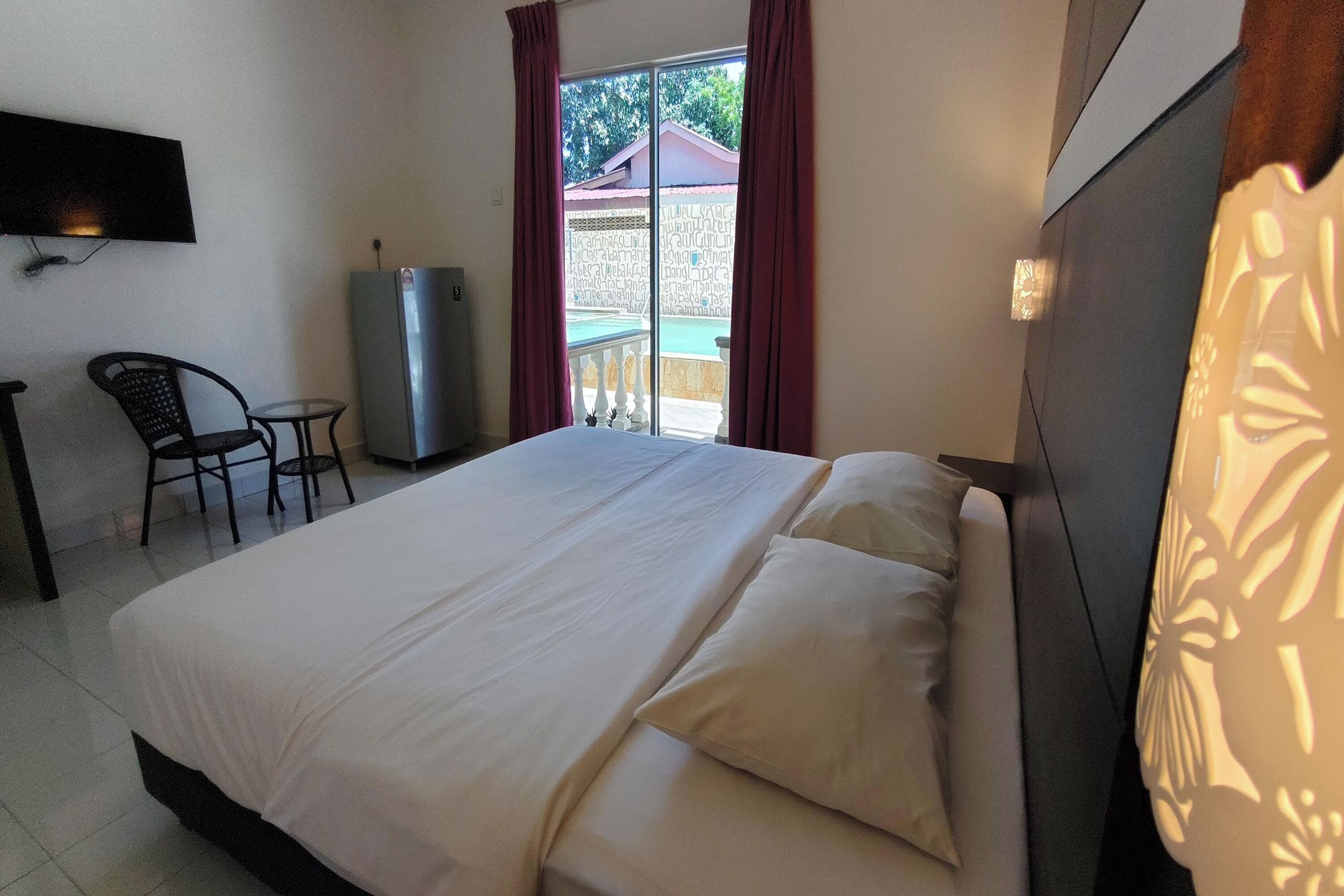 A hotel room with a bed, a desk, a chair, a TV, and a view of the outside.