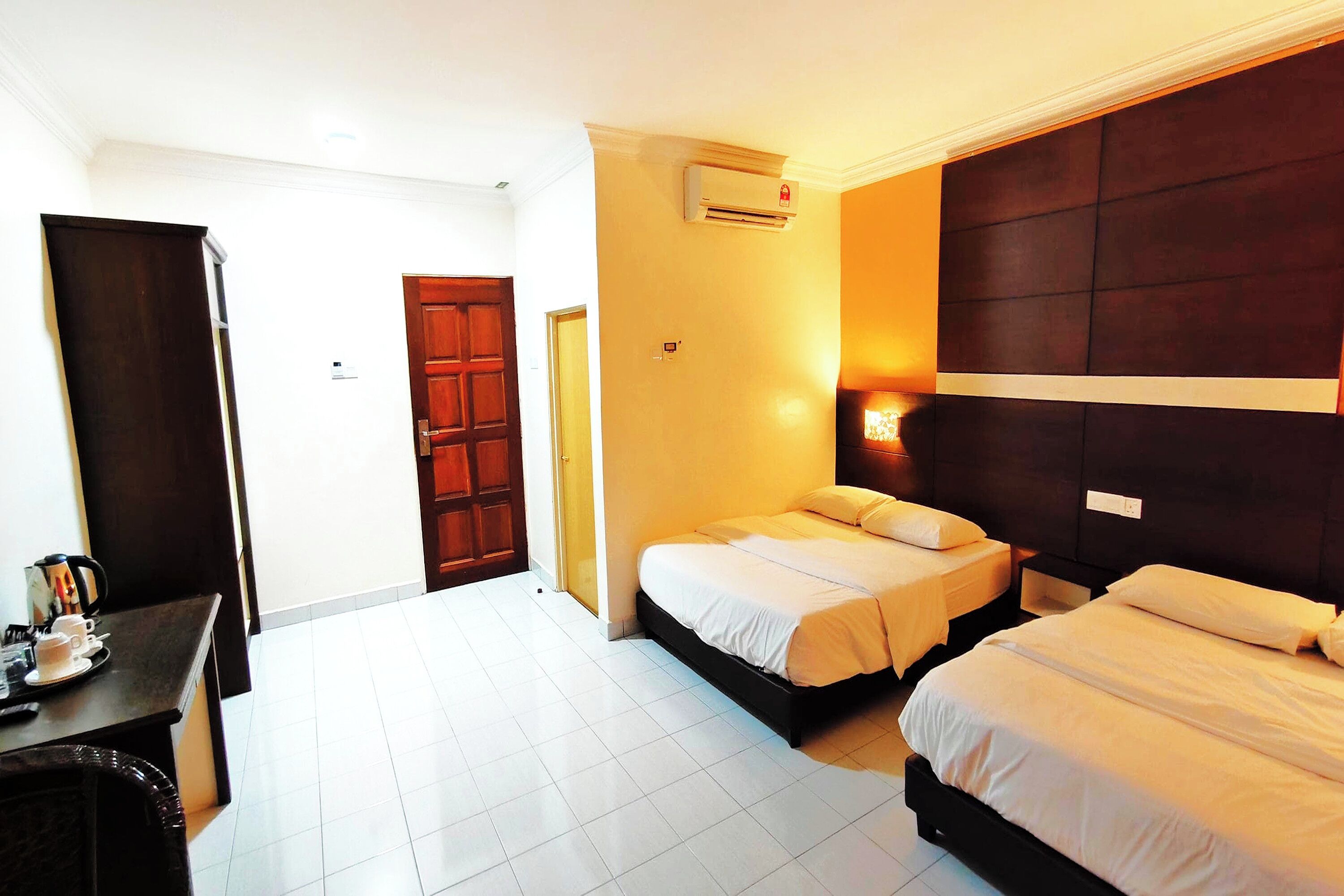 A hotel room with two beds, a desk with a coffee maker, and a wardrobe.