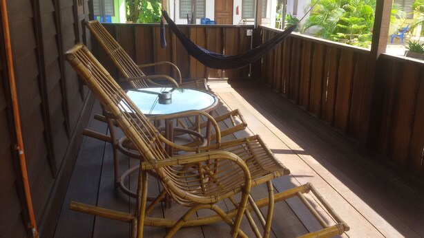 A wooden deck with a table and four wicker chairs, a hammock, and a view of greenery. - Rainbow Lodge Langkawi (Langkawi)