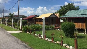 A row of houses with distinct roofs, a paved road, and a grassy area with plants. - Rainbow Lodge Langkawi (Langkawi)