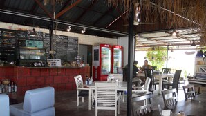 A restaurant with a bar area, white cushioned seating, and a Coca-Cola refrigerator. - Rainbow Lodge Langkawi (Langkawi)