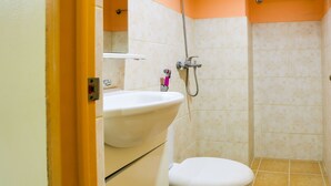 Une salle de bain avec un lavabo, des toilettes et une douche, le tout de couleur blanche.