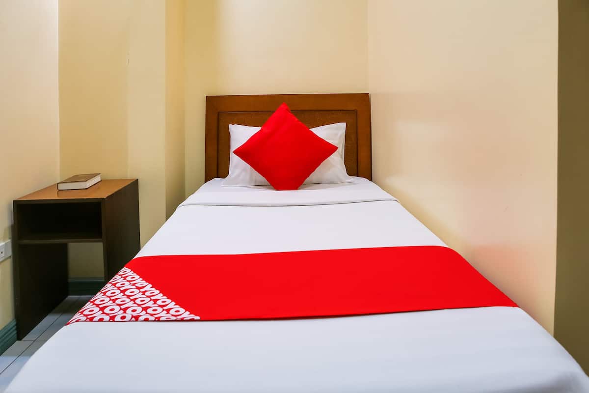 Una cama individual con cabecera de madera, ropa de cama blanca y almohada roja.