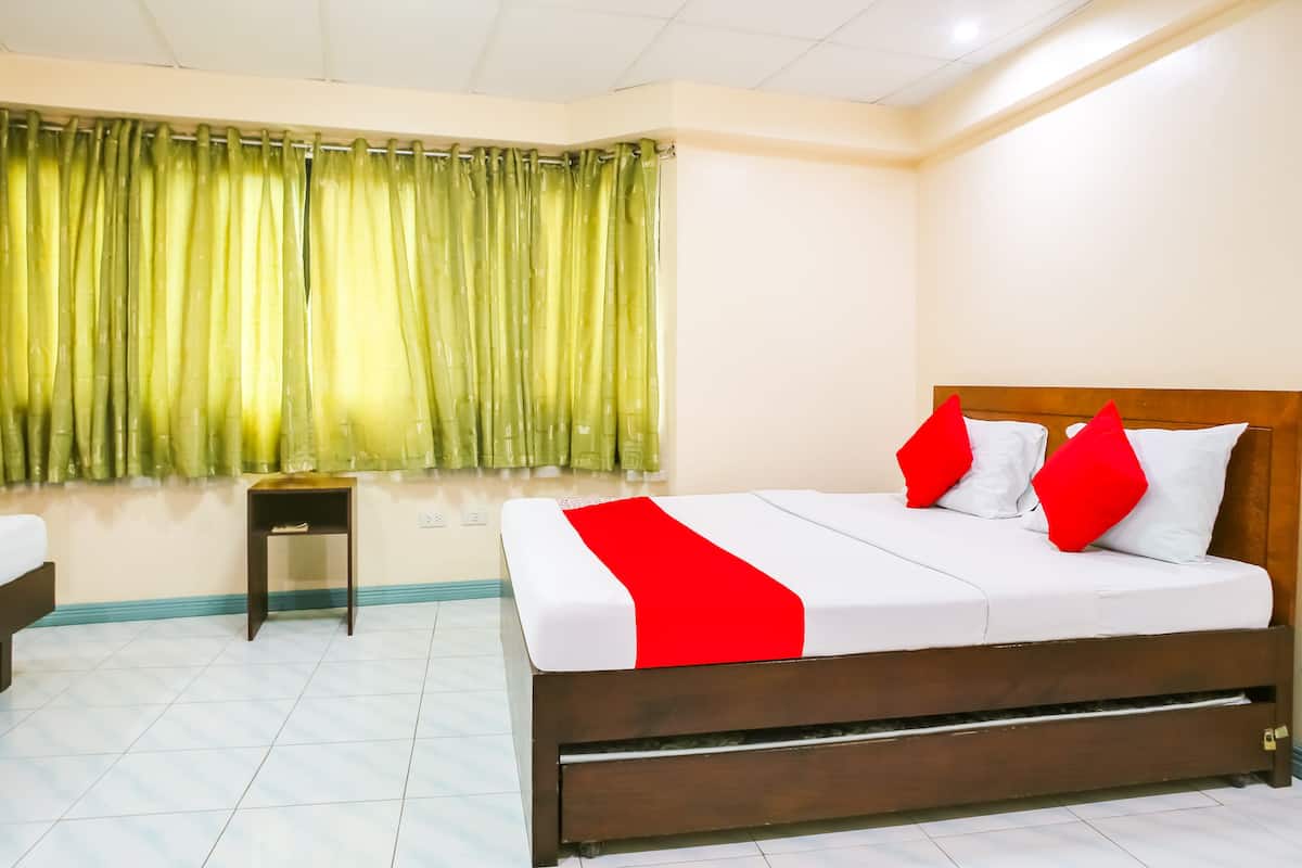 Una habitación de hotel con una cama, una mesita de noche, un ventanal con cortinas verdes y una pared blanca.