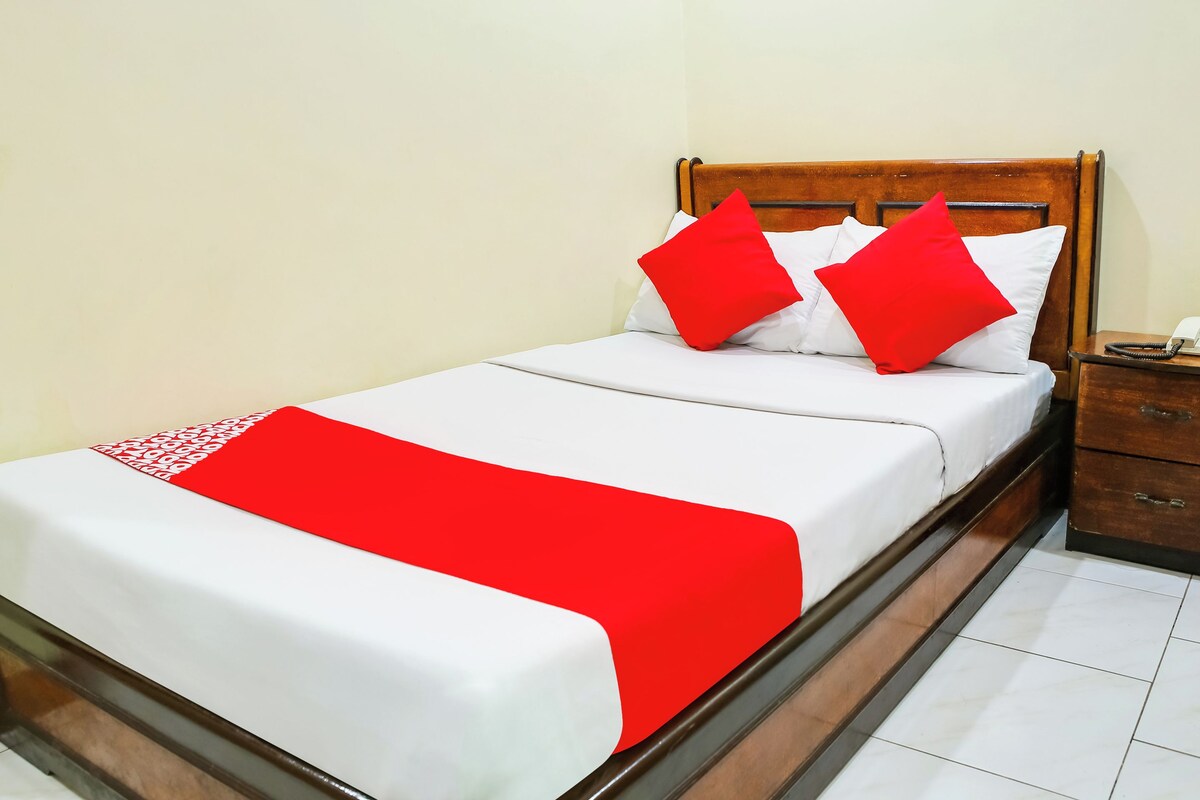 A neatly made bed with white and red bedding, a wooden headboard, and a bedside table with a telephone.