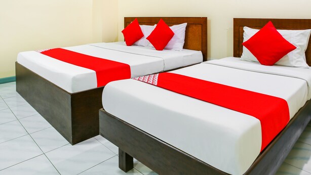 Deux lits simples avec des têtes de lit en bois, du linge de lit blanc et des touches de couleur rouge.