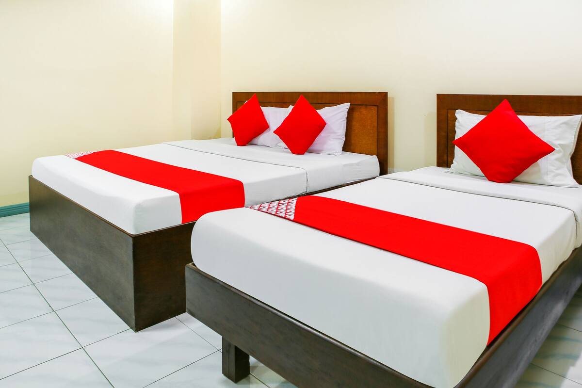 Dos camas individuales con cabeceras de madera, ropa de cama blanca y detalles en rojo.