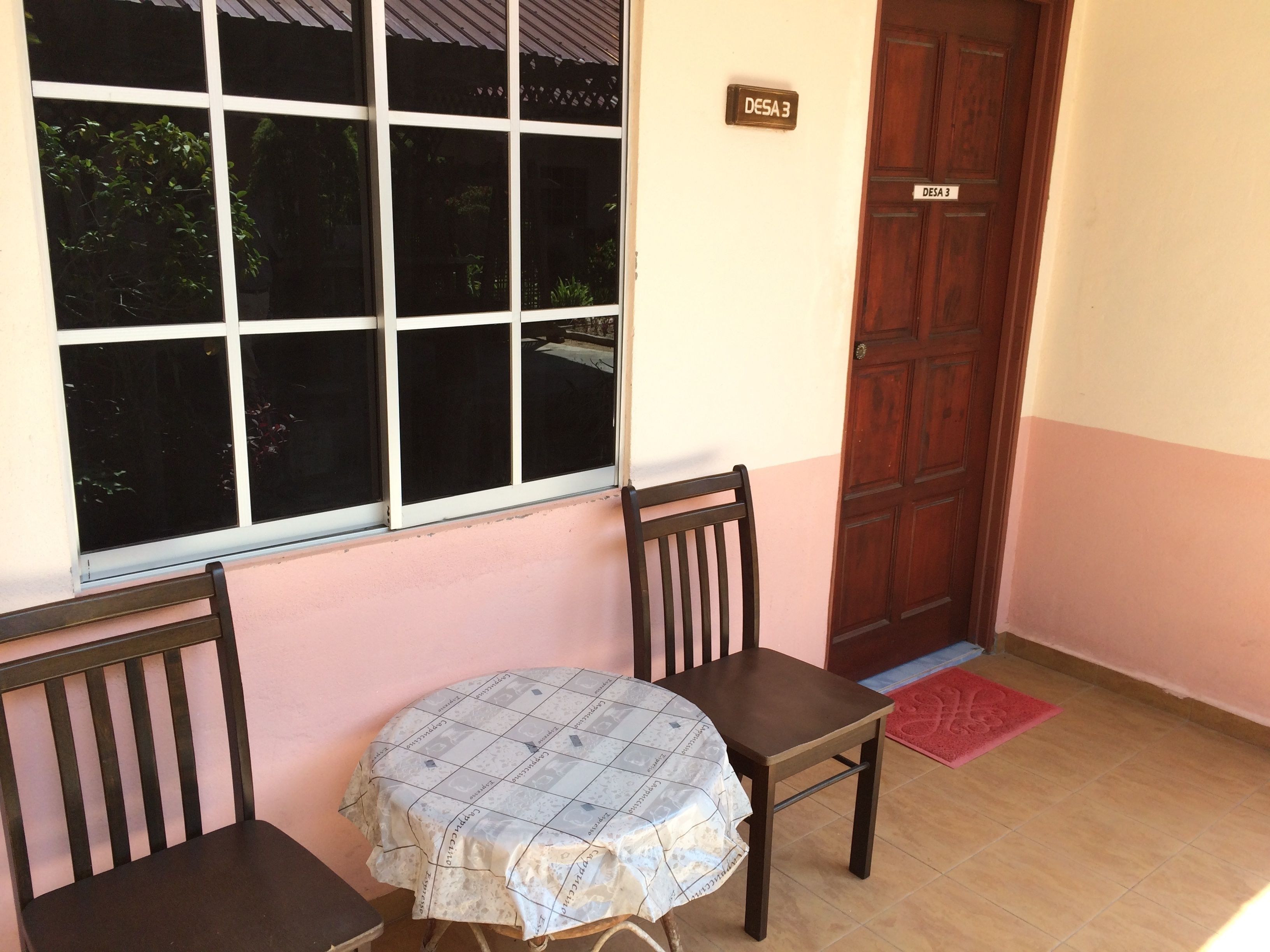 A small room with a table and two chairs, a window, a door, and a nameplate on the wall.