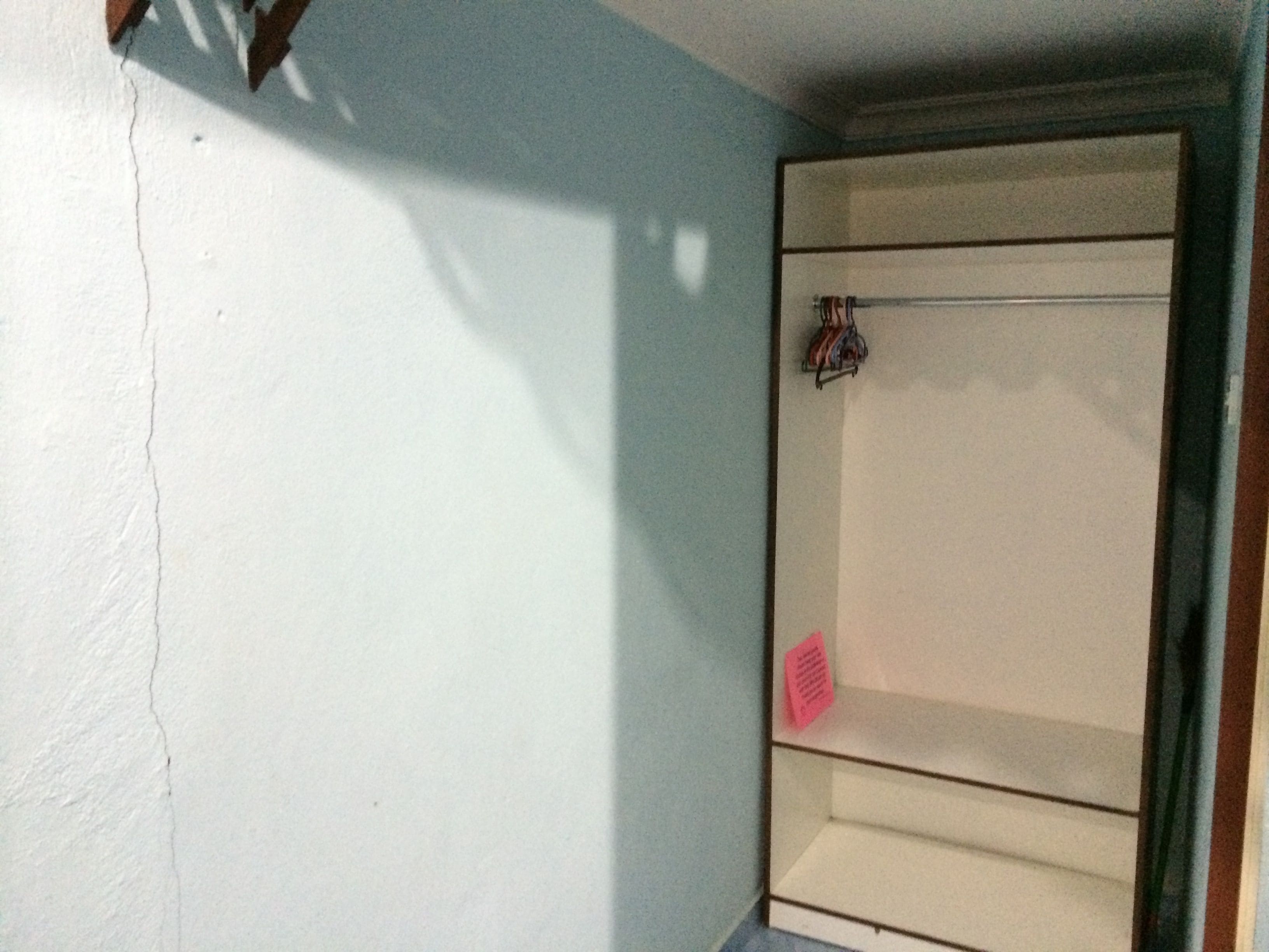 A room with a white wall, a wooden door, and a white cabinet with a small pink note on it.
