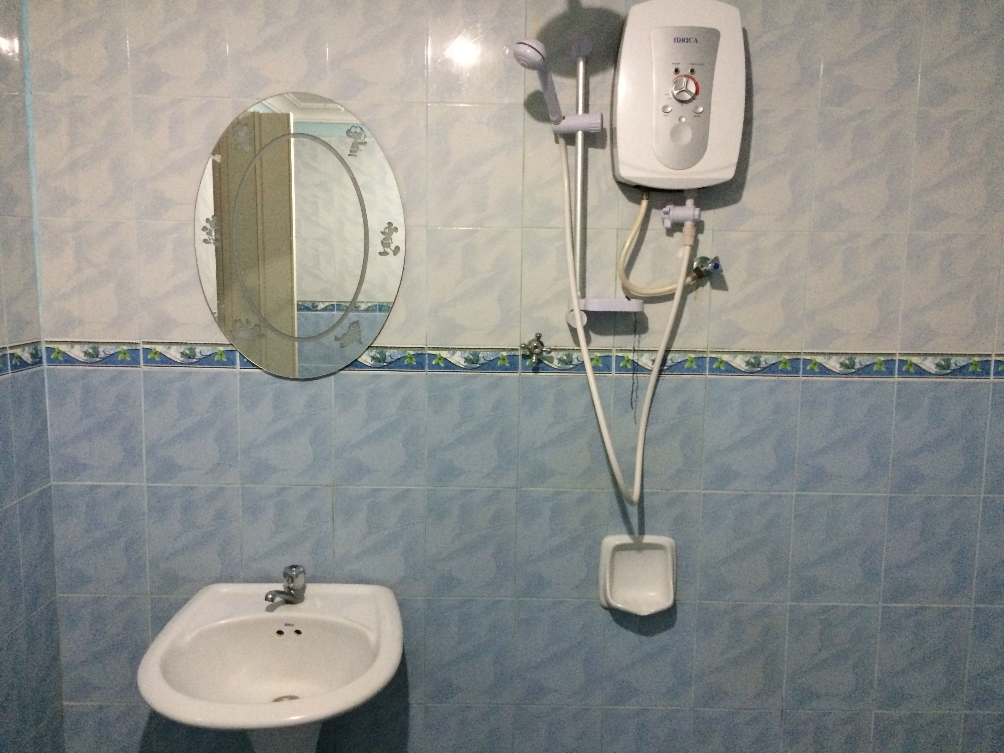 A bathroom with a sink, a mirror, and a wall-mounted shower unit.