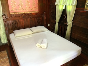 A neatly made bed with white linens and two rolled towels in a wooden room with a floral-patterned headboard and green curtains. - Desa Motel (Langkawi)
